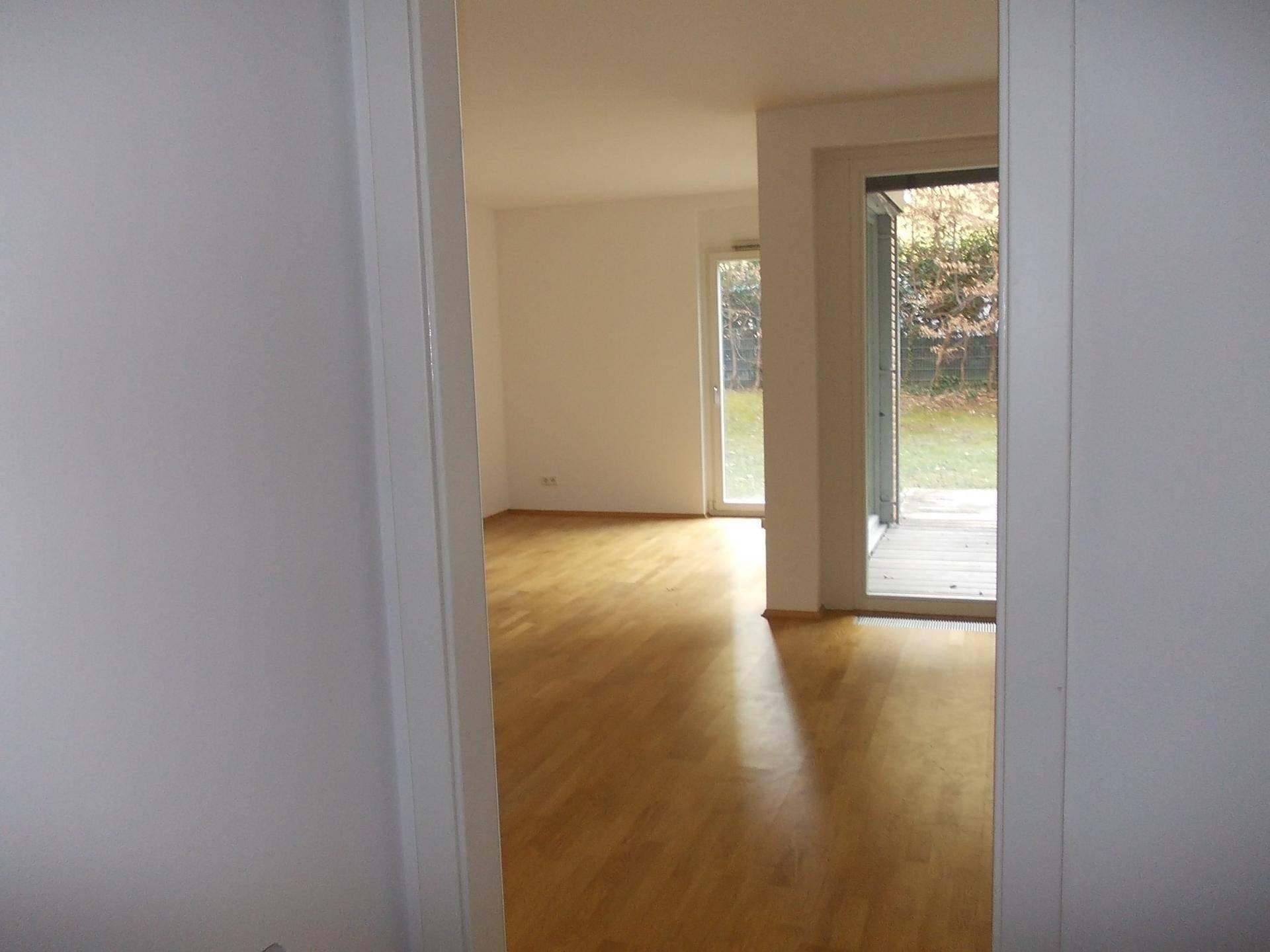 Heller Wohnbereich mit Parkettboden und großen Fenstern, die den Blick in den Garten freigeben.