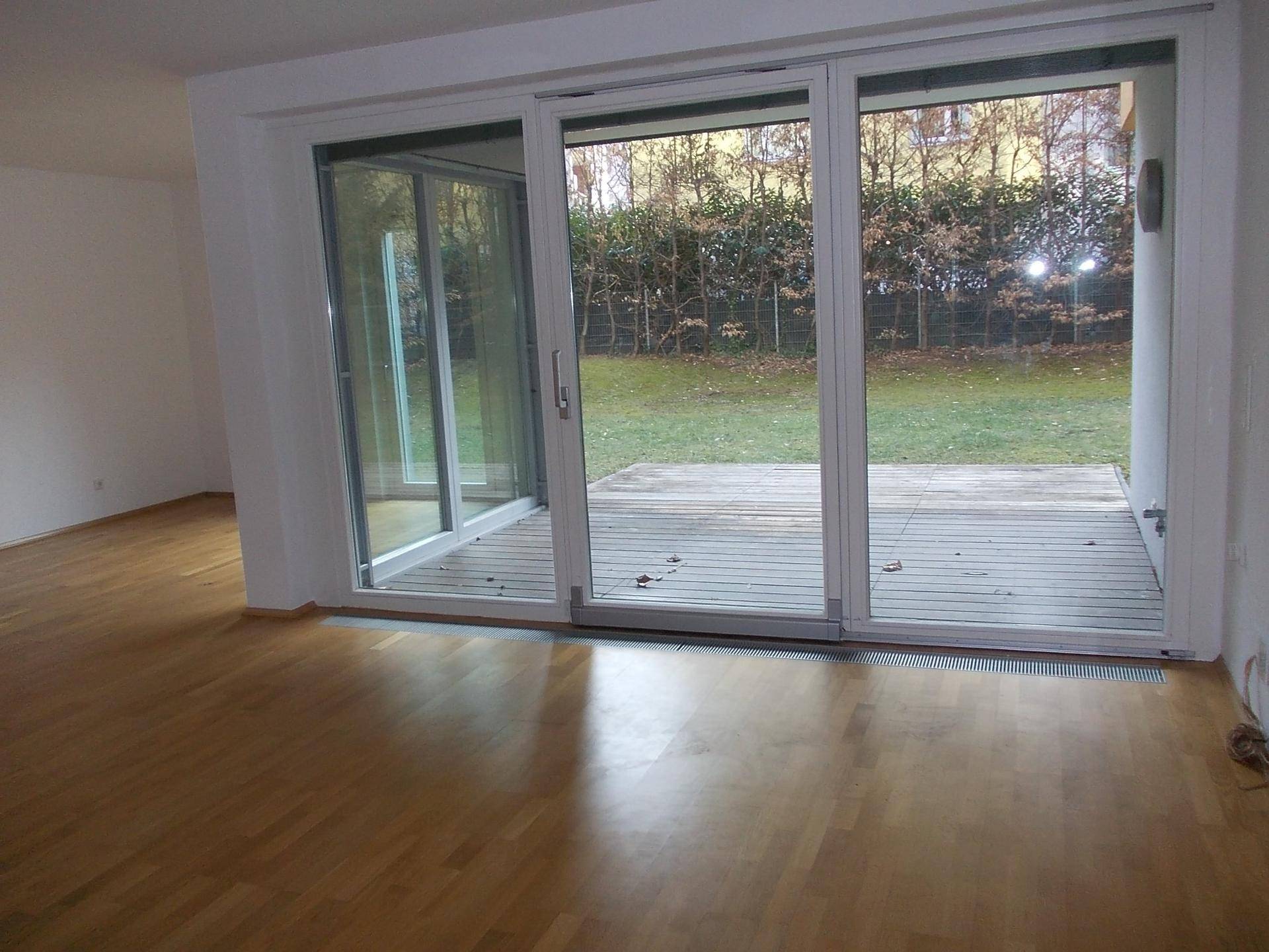 Lichtdurchfluteter Wohnbereich mit Parkettboden und breiter Schiebetür zur Holzterrasse.