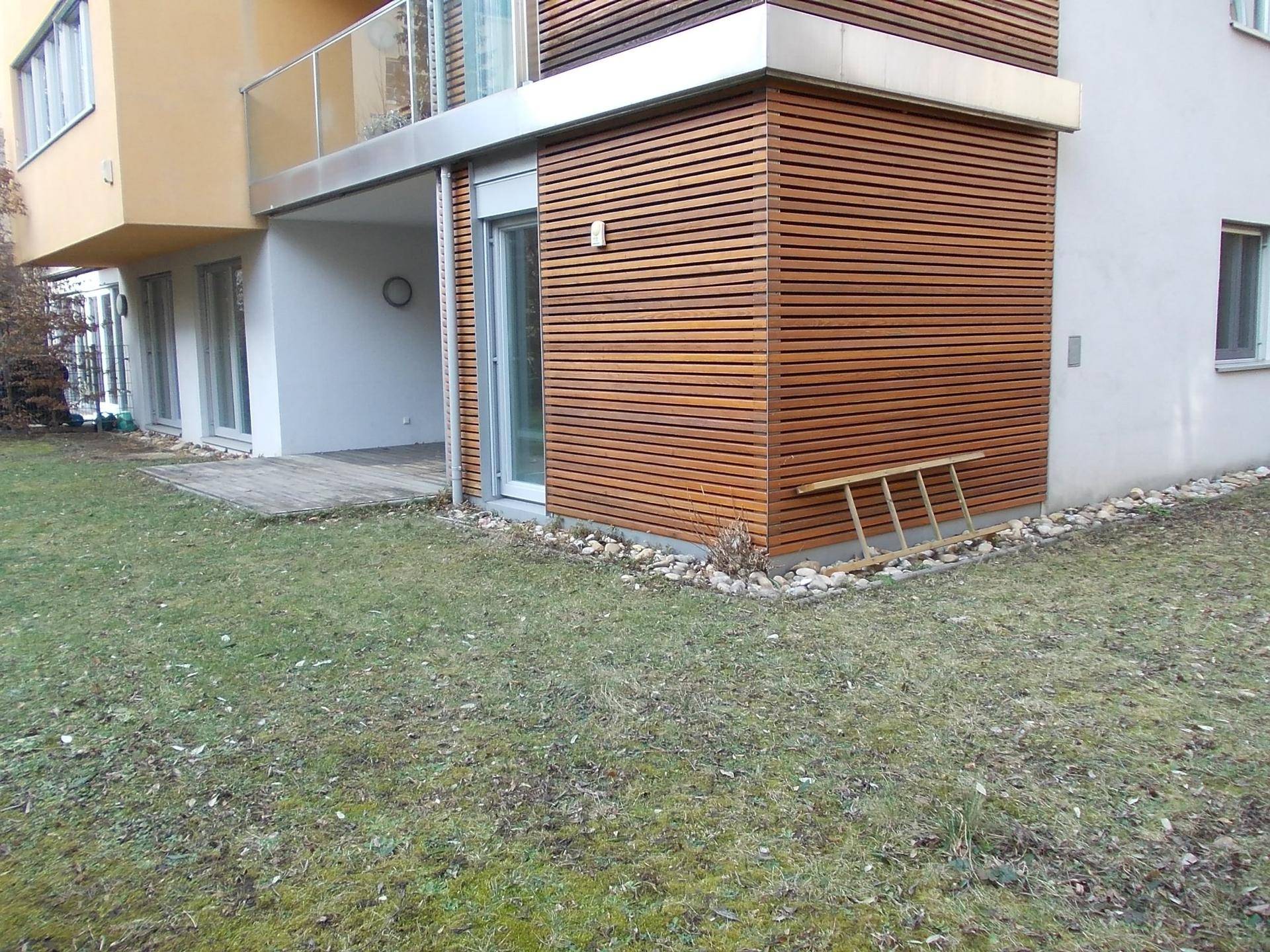 Seitlicher Blick auf die moderne Gebäudefassade mit Holzverkleidung und direktem Zugang zum Garten.