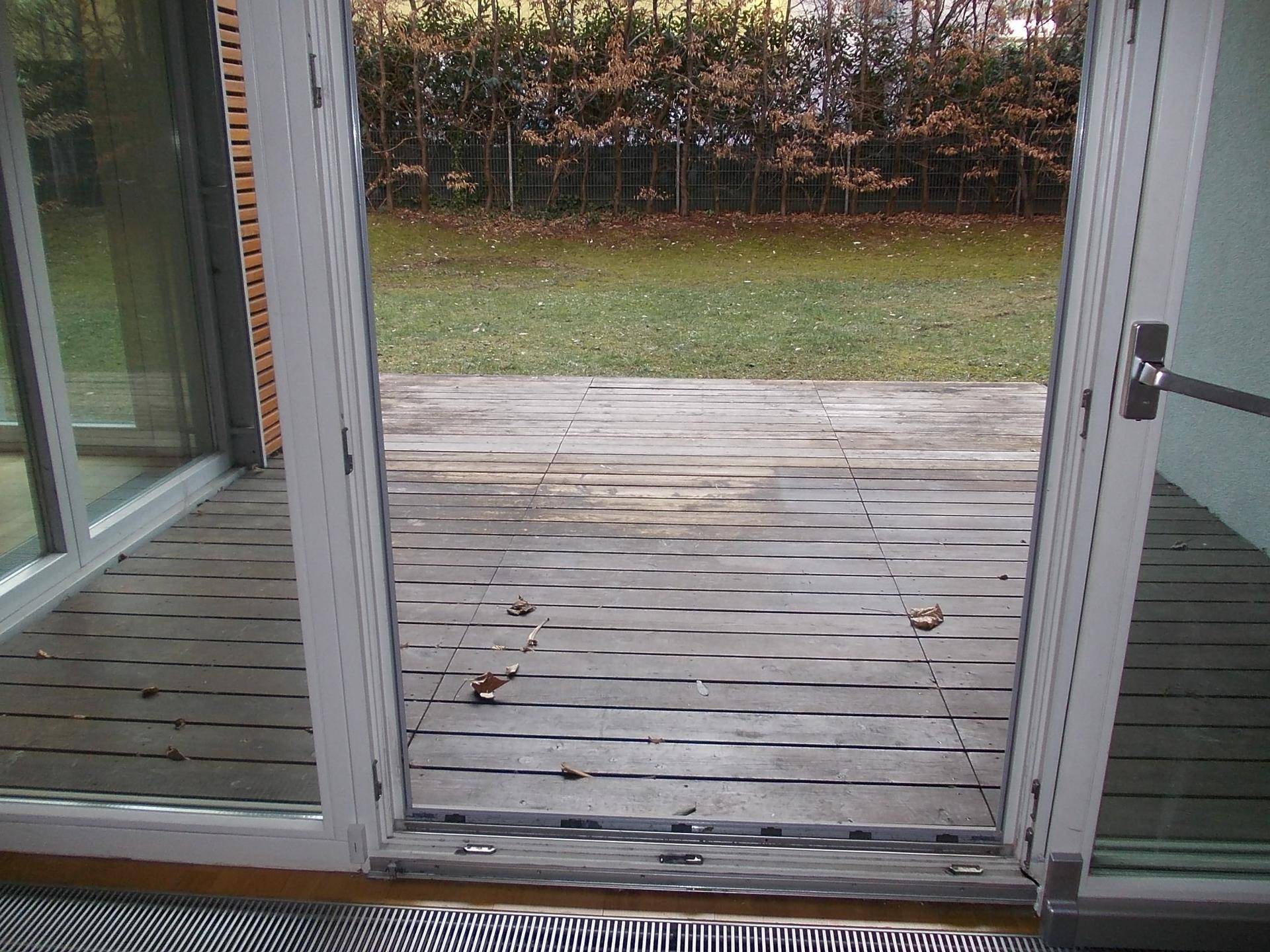 Blick von innen auf die Holzterrasse und den dahinterliegenden grünen Gartenbereich.