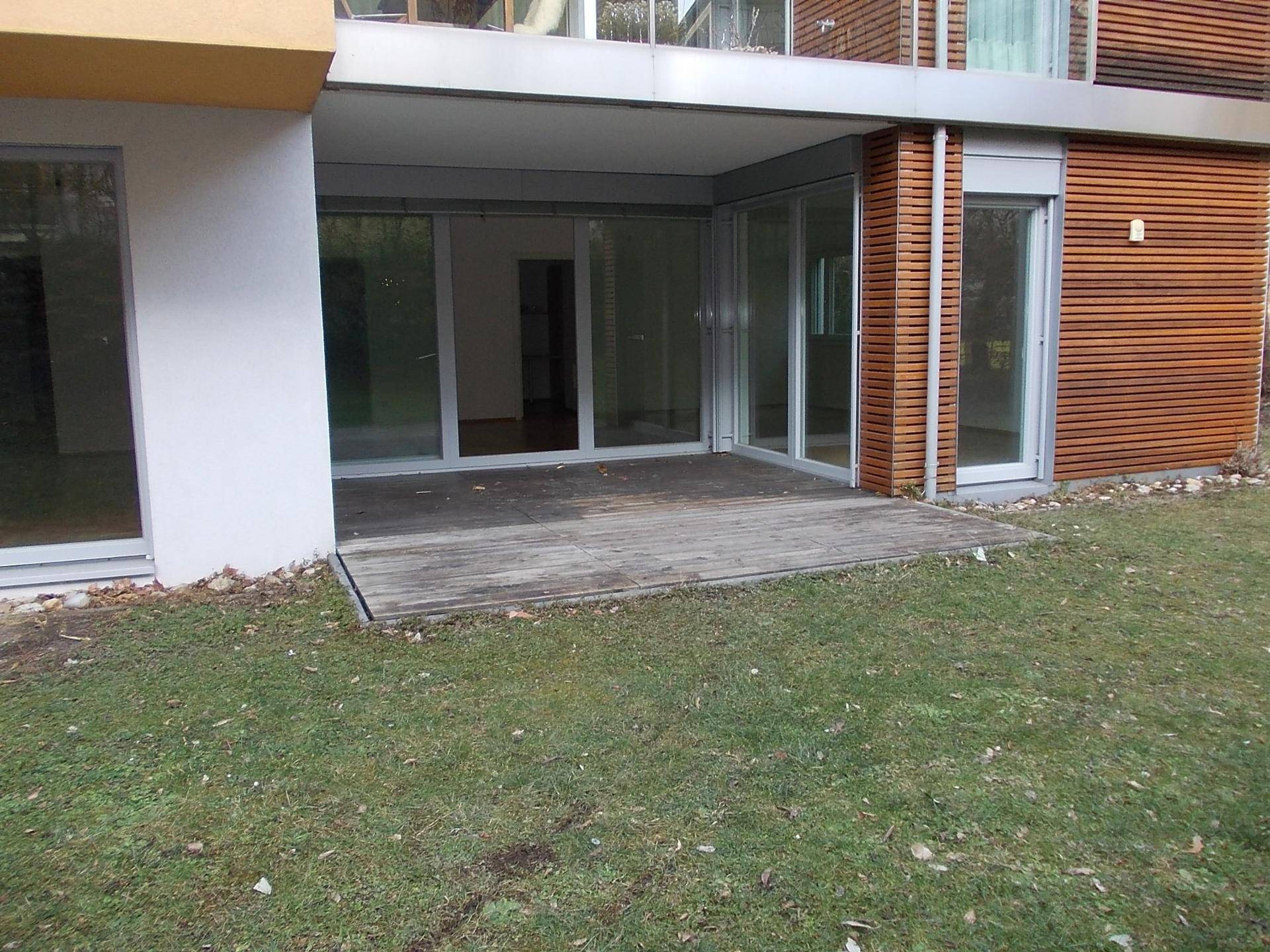 Gartenbereich mit Rasenfläche und einer kleinen Holzterrasse vor dem modernen Gebäude.