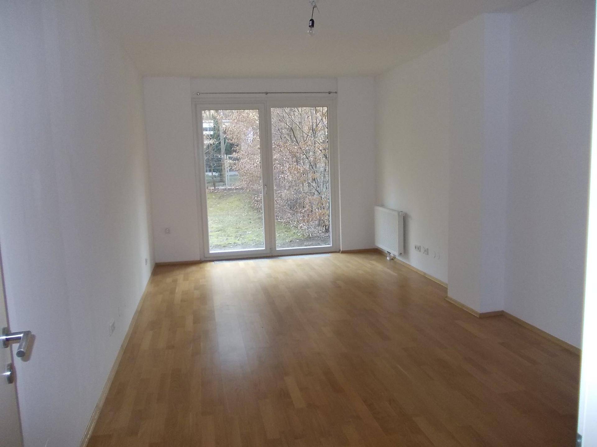 Helles Zimmer mit Parkettboden und großer Fenstertür, die Zugang zum Außenbereich bietet.
