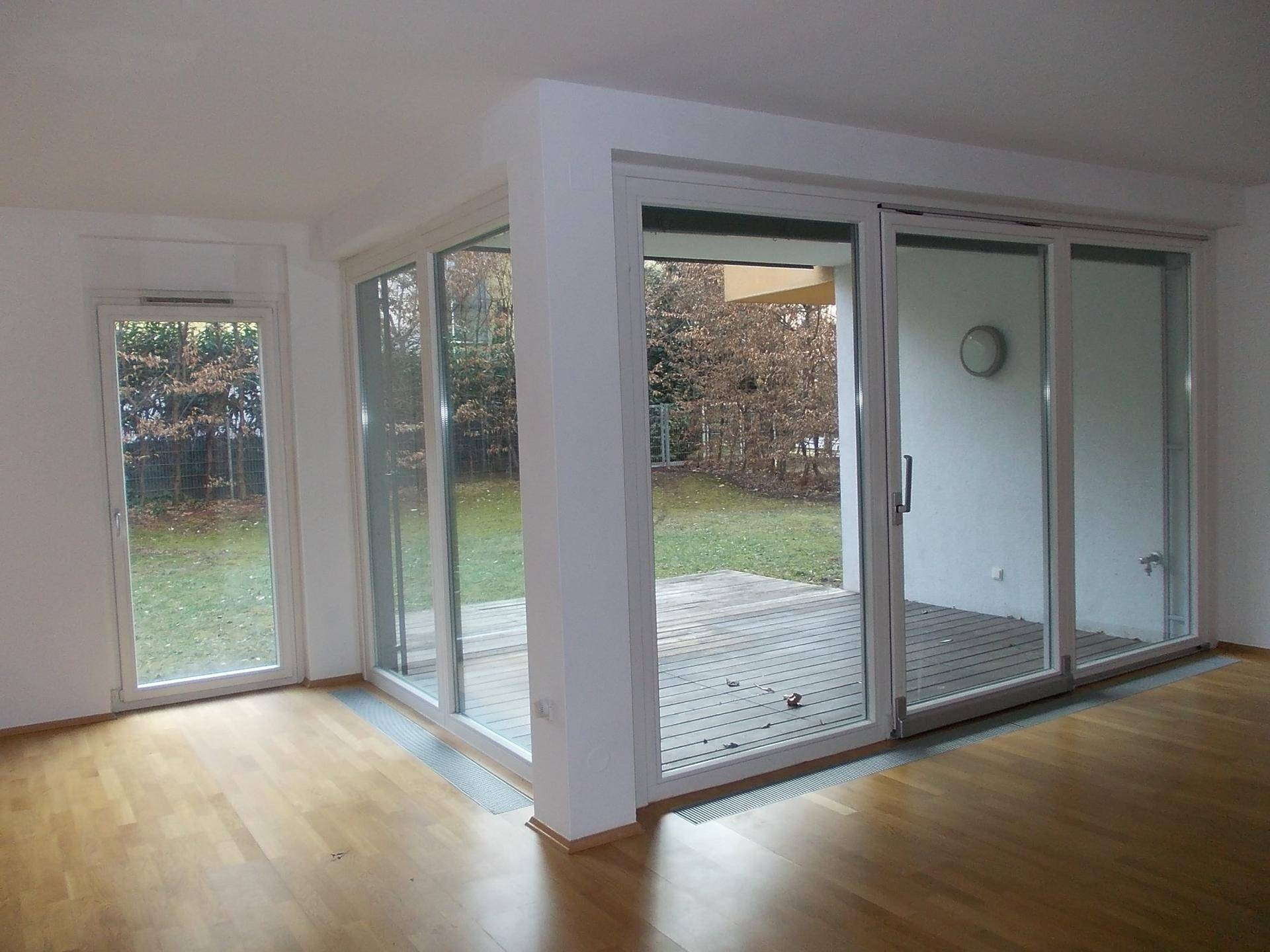 Heller Wohnbereich mit Parkettboden und großen Glasfronten, die viel Licht und Gartenblick bieten.