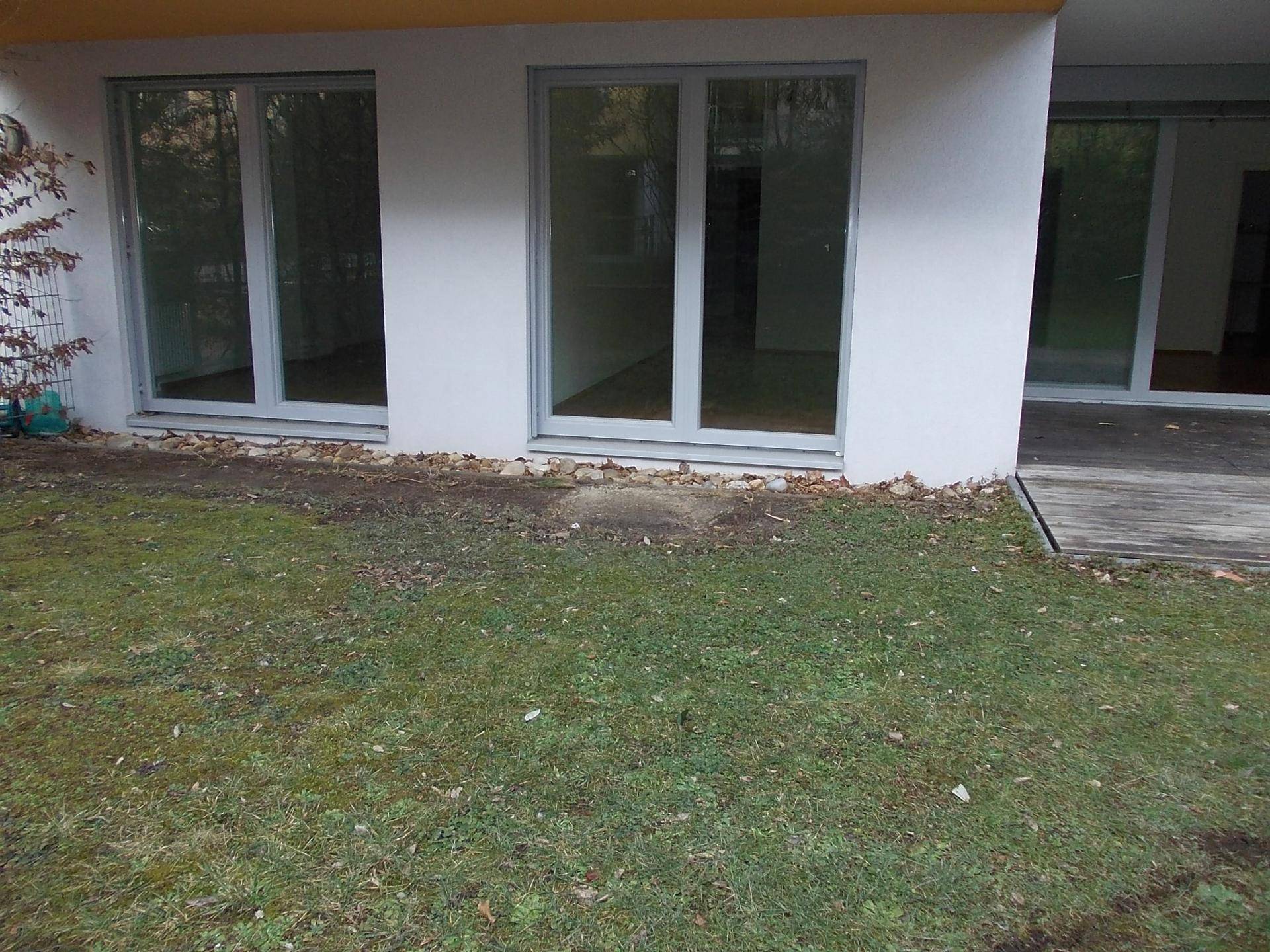 Gartenansicht mit Rasenfläche und großen Fenstern im Erdgeschoss des modernen Gebäudes.