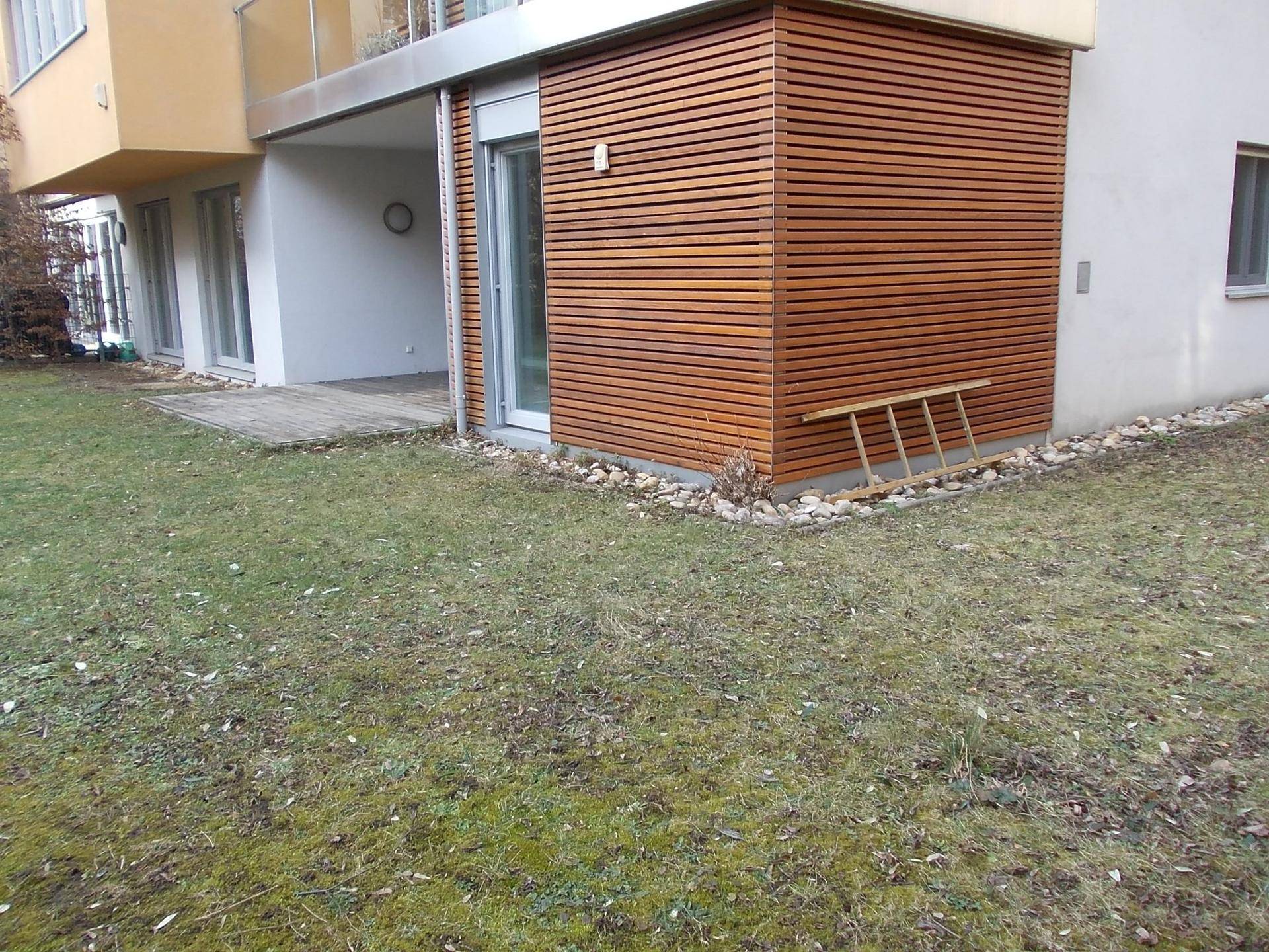 Seitlicher Blick auf die moderne Gebäudefassade mit Holzverkleidung und direktem Zugang zum Garten.