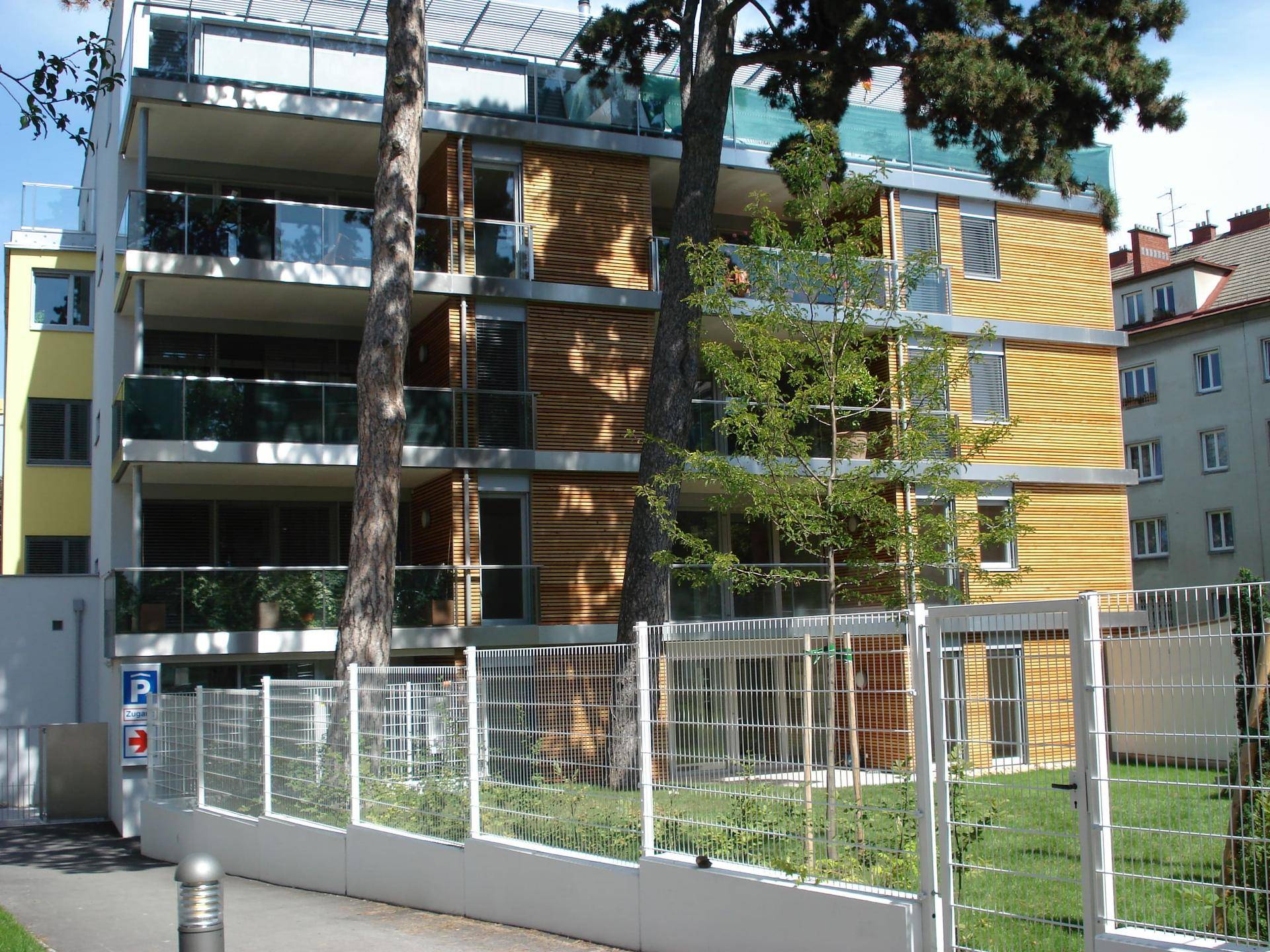 Moderne Wohnanlage mit mehreren Balkonen, Glasgeländern und Holzverkleidung der Fassade.