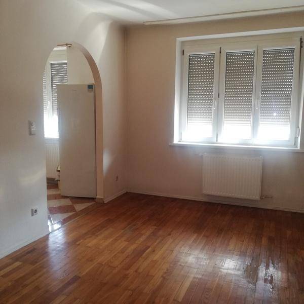 Geräumiges Wohnzimmer mit hellem Parkettboden und großen Fenstern, die viel Tageslicht hereinlassen.