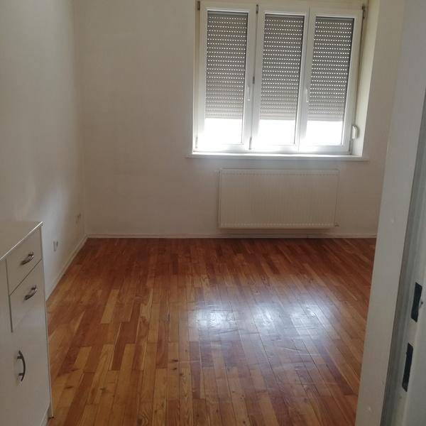 Helles Zimmer mit Parkettboden und großen Fenstern, ideal als Schlaf- oder Arbeitszimmer.