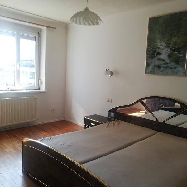Schlafzimmer mit Doppelbett, Parkettboden und einem Fenster, das Tageslicht hereinlässt.