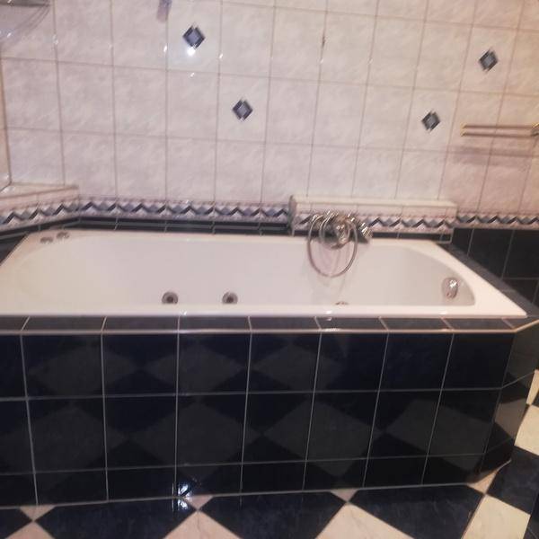 Badezimmer mit eingebauter Badewanne und dunkelblauen sowie weißen Fliesen.