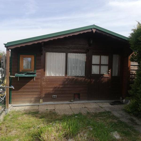 Nahaufnahme der Holzfassade eines kleinen Hauses mit grüner Dachkante und Fenstern mit weißen Vorhängen.