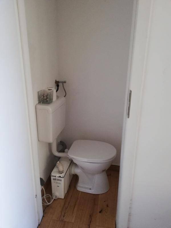 Kleine separate Toilette mit WC und Holzboden, in einem schlichten und funktionalen Design.