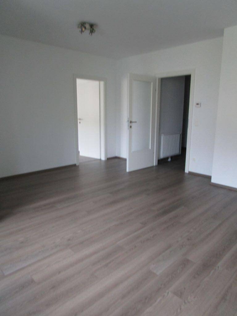 Geräumiges, leeres Zimmer mit Laminatboden und weißen Wänden, bereit zur individuellen Gestaltung.