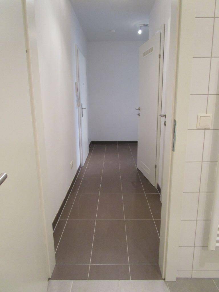 Langer, heller Flur mit grauen Fliesen und weißen Türen, der zu weiteren Räumen führt.