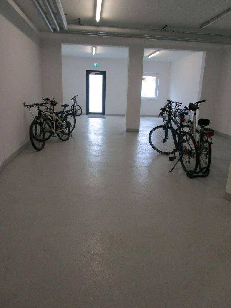Heller Fahrradraum im Untergeschoss mit mehreren abgestellten Fahrrädern und Fliesenboden.