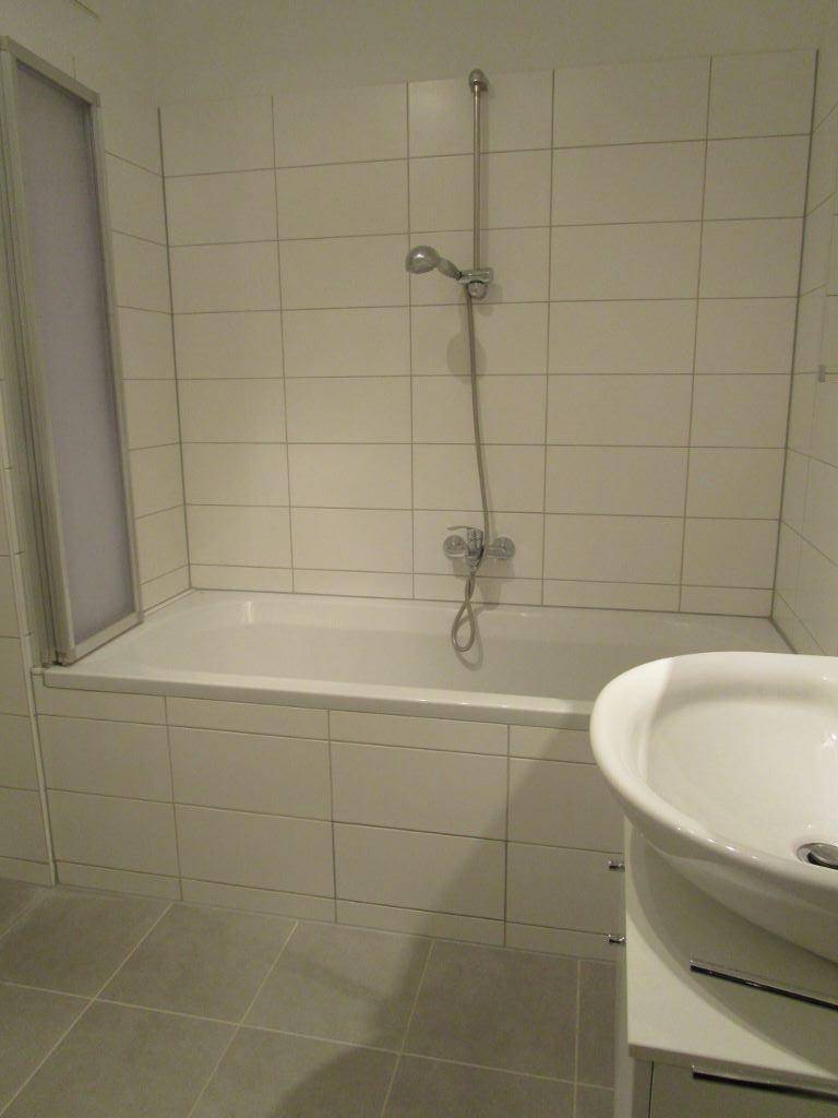 Helles Badezimmer mit Badewanne, Duscharmatur und Waschbecken mit Unterschrank.