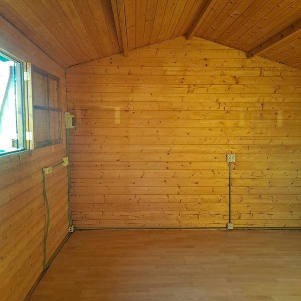 Leerer Innenraum einer Holzhütte mit Holzwänden, Laminatboden und schrägen Decken.