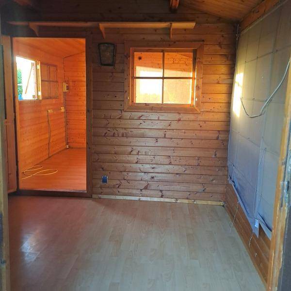 Innenansicht einer Holzhütte mit Holzwänden, Laminatboden und warmem Licht durch die Fenster.
