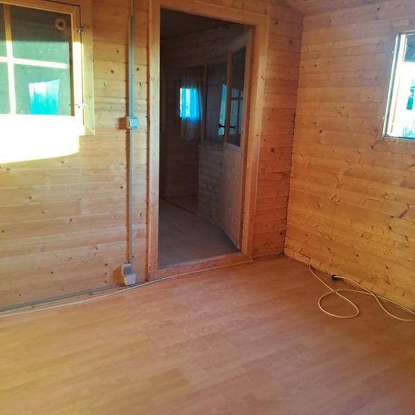 Innenansicht einer Holzhütte mit Holzwänden, Laminatboden und einem Durchgang zu einem weiteren Raum.