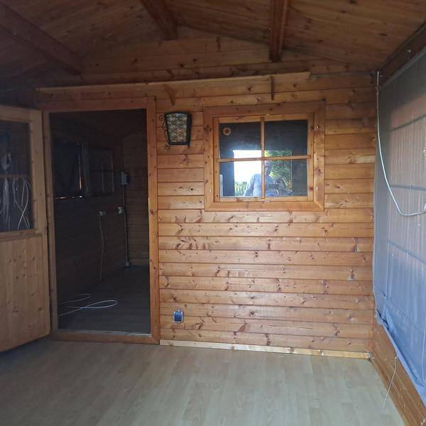 Innenraum einer Holzhütte mit Holzwänden, Laminatboden und einer Holztür zu einem Nebenraum.