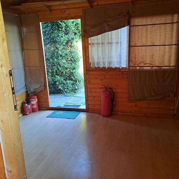 Innenraum einer Holzhütte mit Holzwänden, Laminatboden und Blick ins Grüne durch die offene Tür.