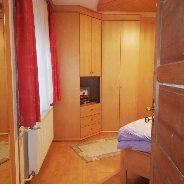 Schlafzimmer mit Einbauschränken aus hellem Holz und einem Fenster mit rotem Vorhang.