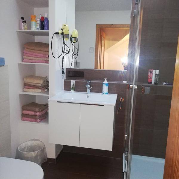 Modernes Badezimmer mit Duschkabine, Waschbecken und praktischen Ablageflächen für Handtücher und Pflegeprodukte.