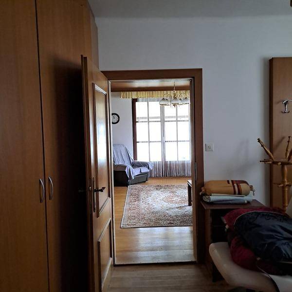 Flur mit Holztüren und Blick in ein helles Wohnzimmer mit Parkettboden und großem Fenster.