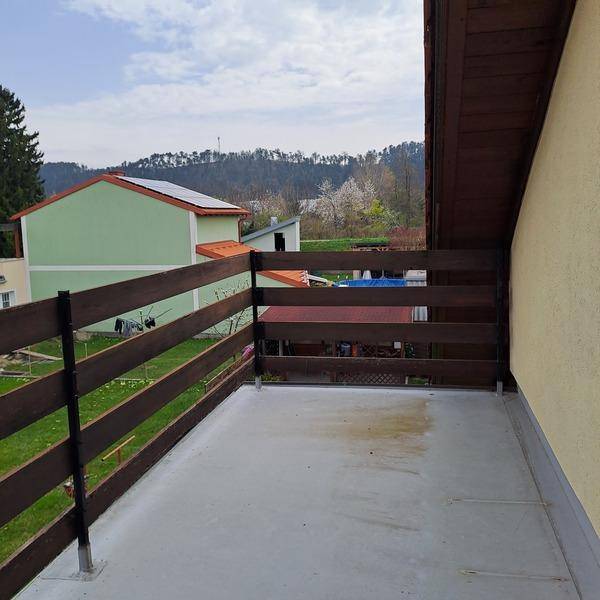 Balkon mit Holzzaun und Blick auf die umliegende grüne Landschaft und Berge.