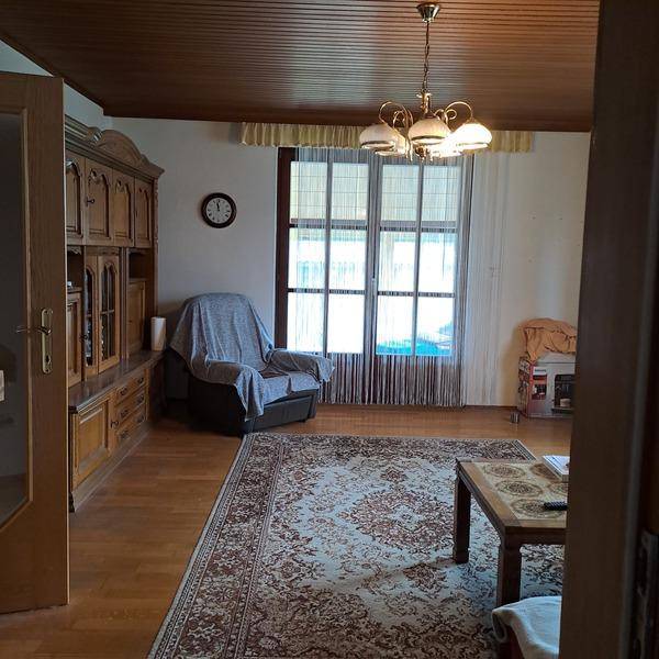 Geräumiges Wohnzimmer mit Holzdecke, Parkettboden, großem Fenster und traditionellen Möbeln.