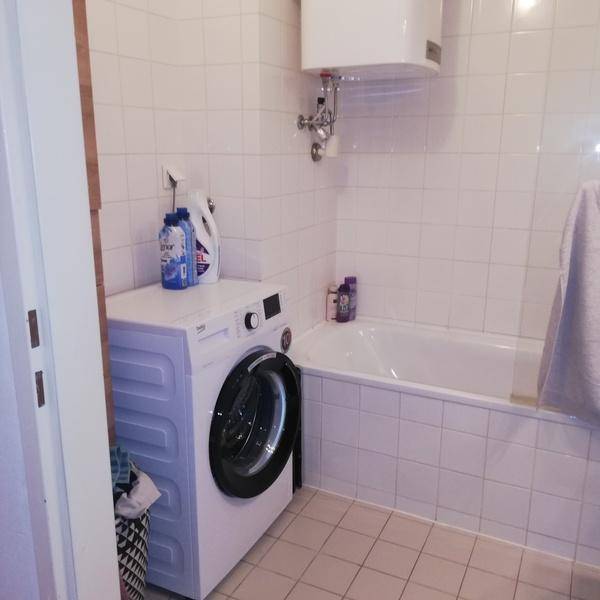 Badezimmer mit Badewanne, Waschmaschine und weißen Wand- und Bodenfliesen.