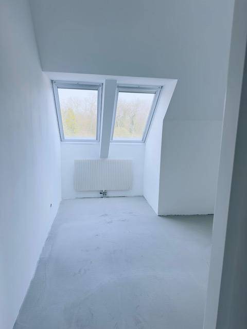 Dachgeschossraum mit zwei Dachfenstern, Heizkörper und schrägen Wänden.
