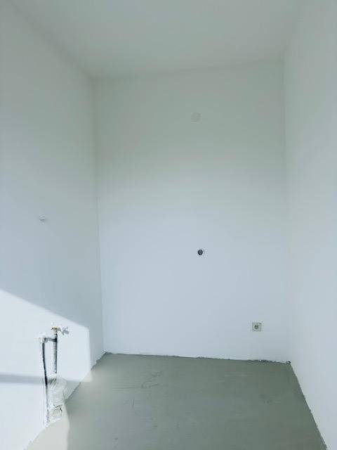 Leerer Raum mit weißen Wänden und Betonboden, bereit für den Ausbau.