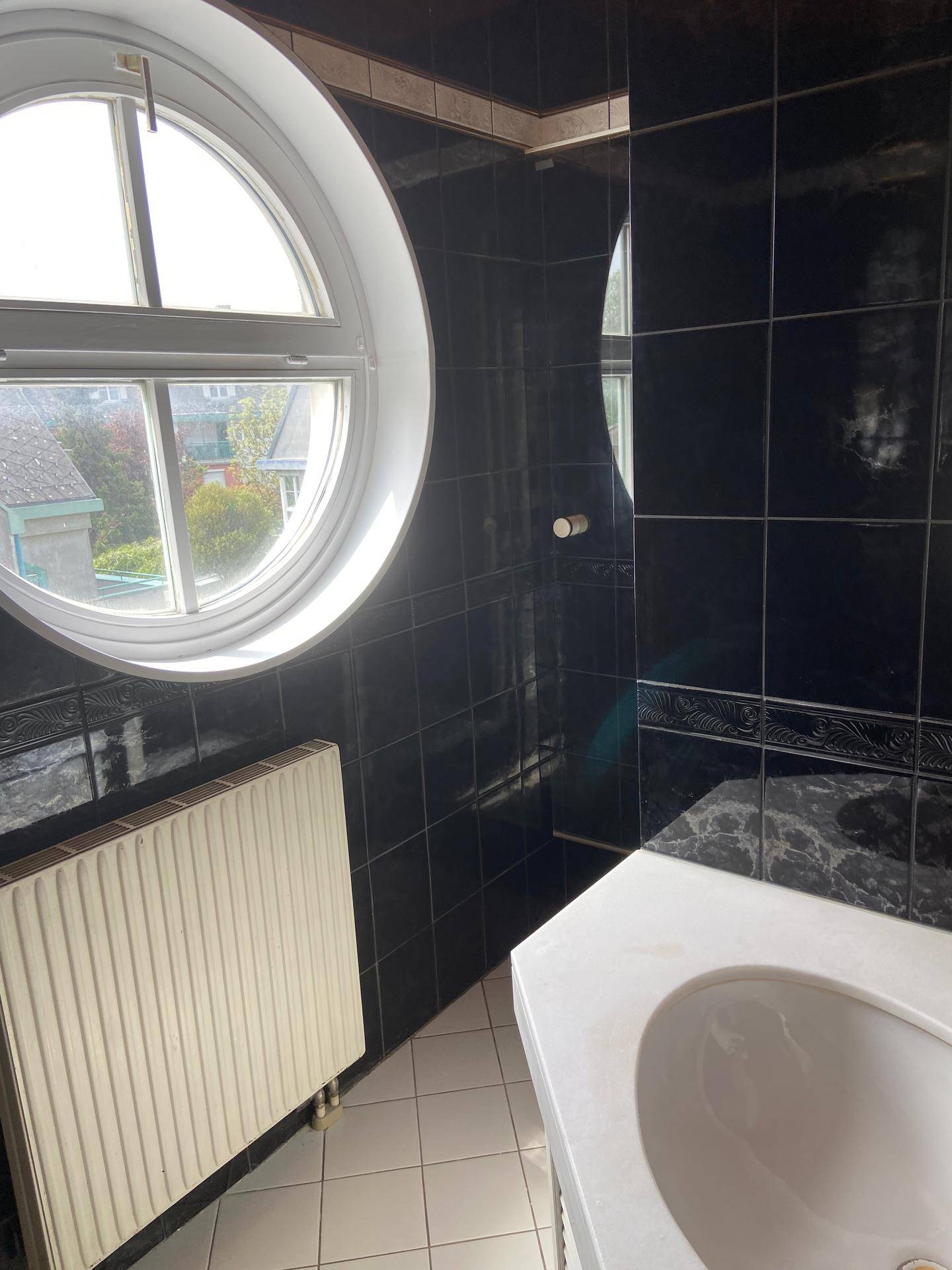 Badezimmer mit dunklen Fliesen, rundem Fenster und Heizkörper.