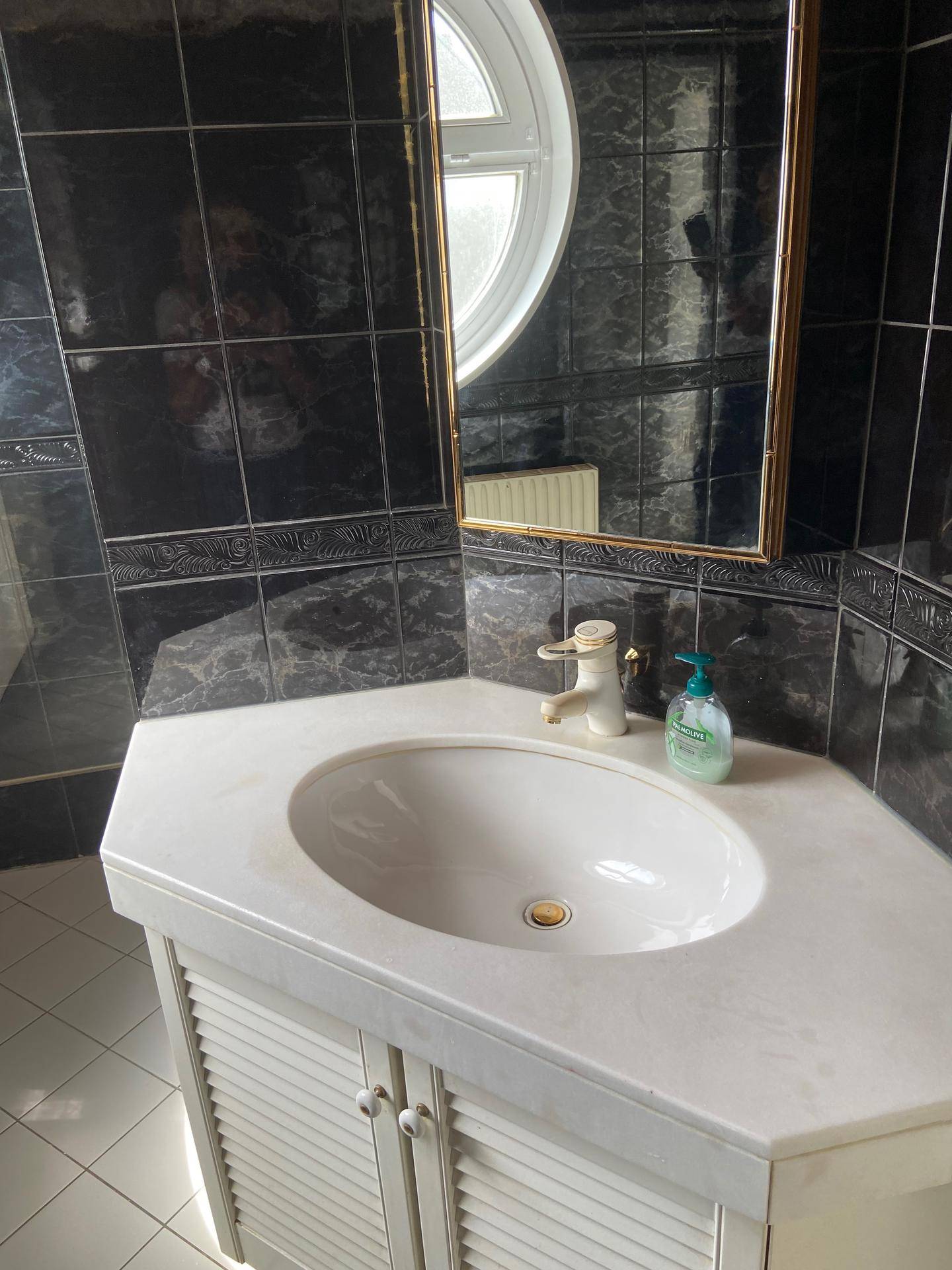 Waschtisch mit weißem Waschbecken, Spiegelschrank und dunklen Wandfliesen.