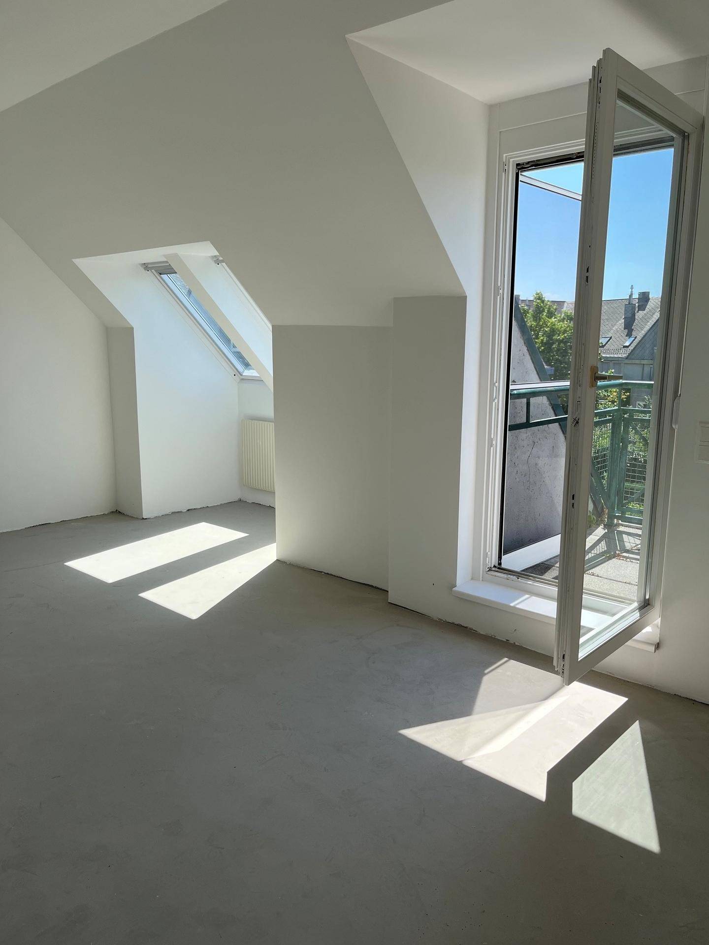Heller Raum im Dachgeschoss mit Zugang zu einem Balkon und Dachfenster.