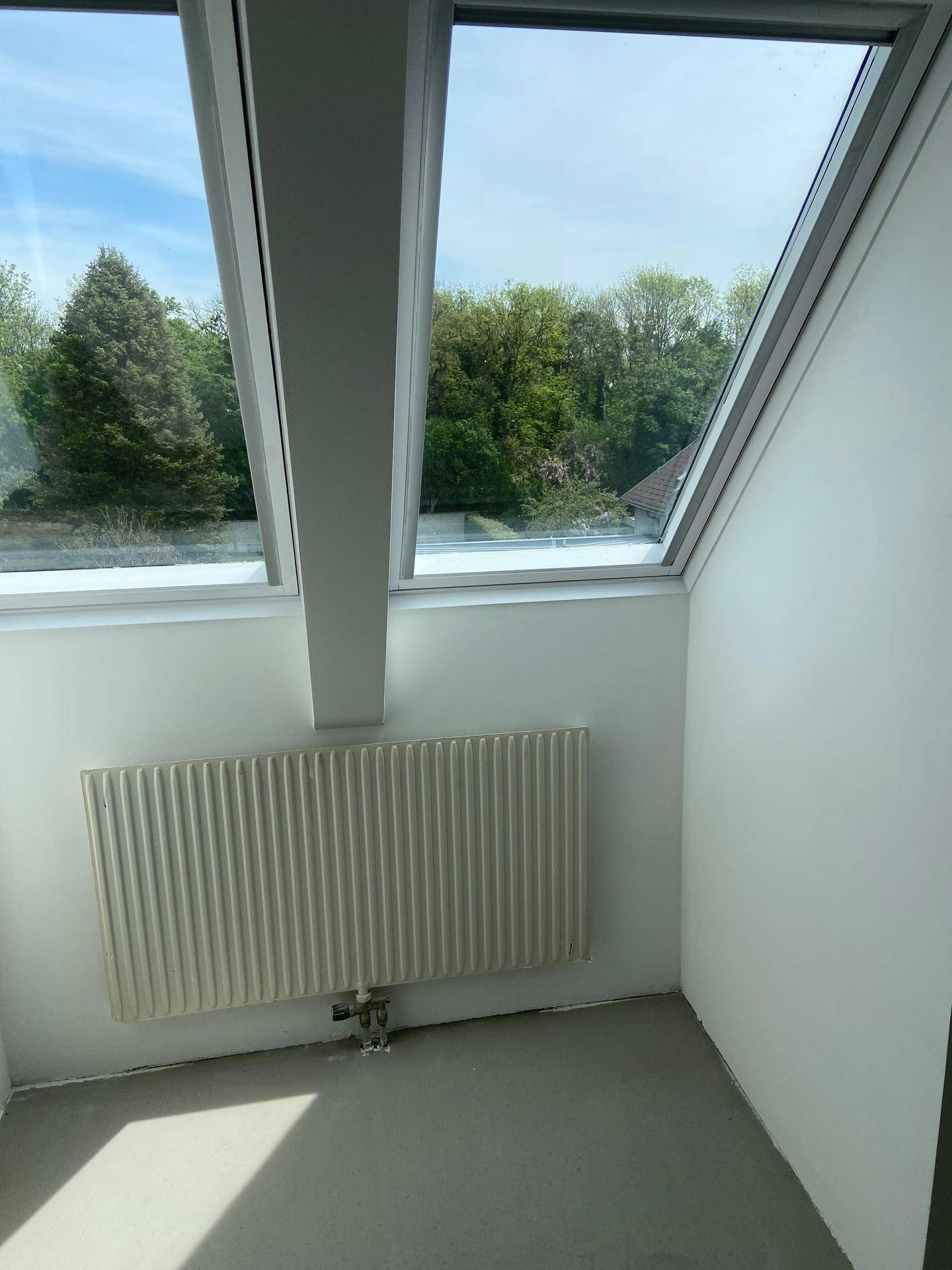 Heller Dachgeschossraum mit zwei Dachfenstern, Heizkörper und Blick ins Grüne.
