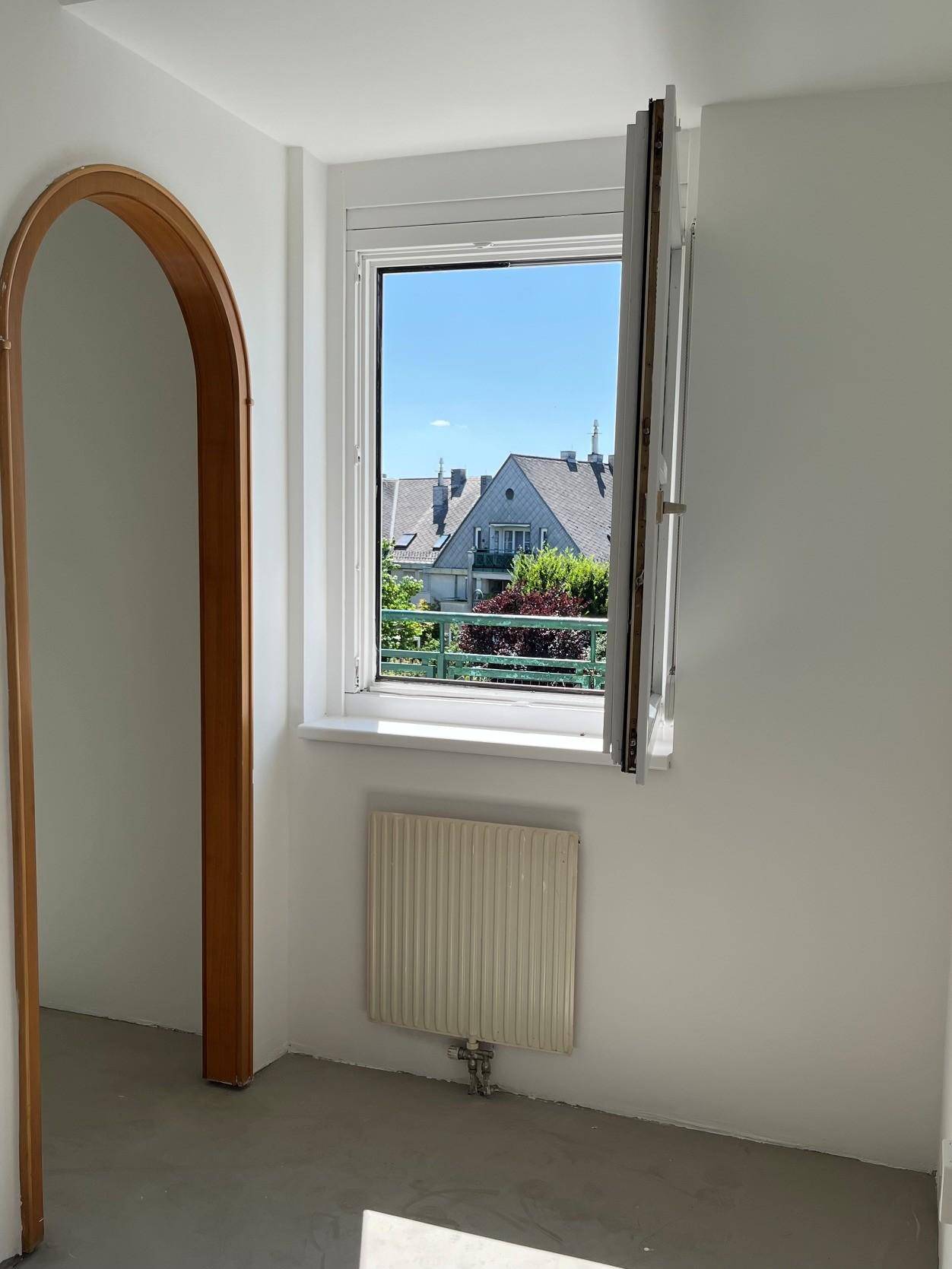 Heller Raum mit Fenster, Heizkörper und einem dekorativen Rundbogen.