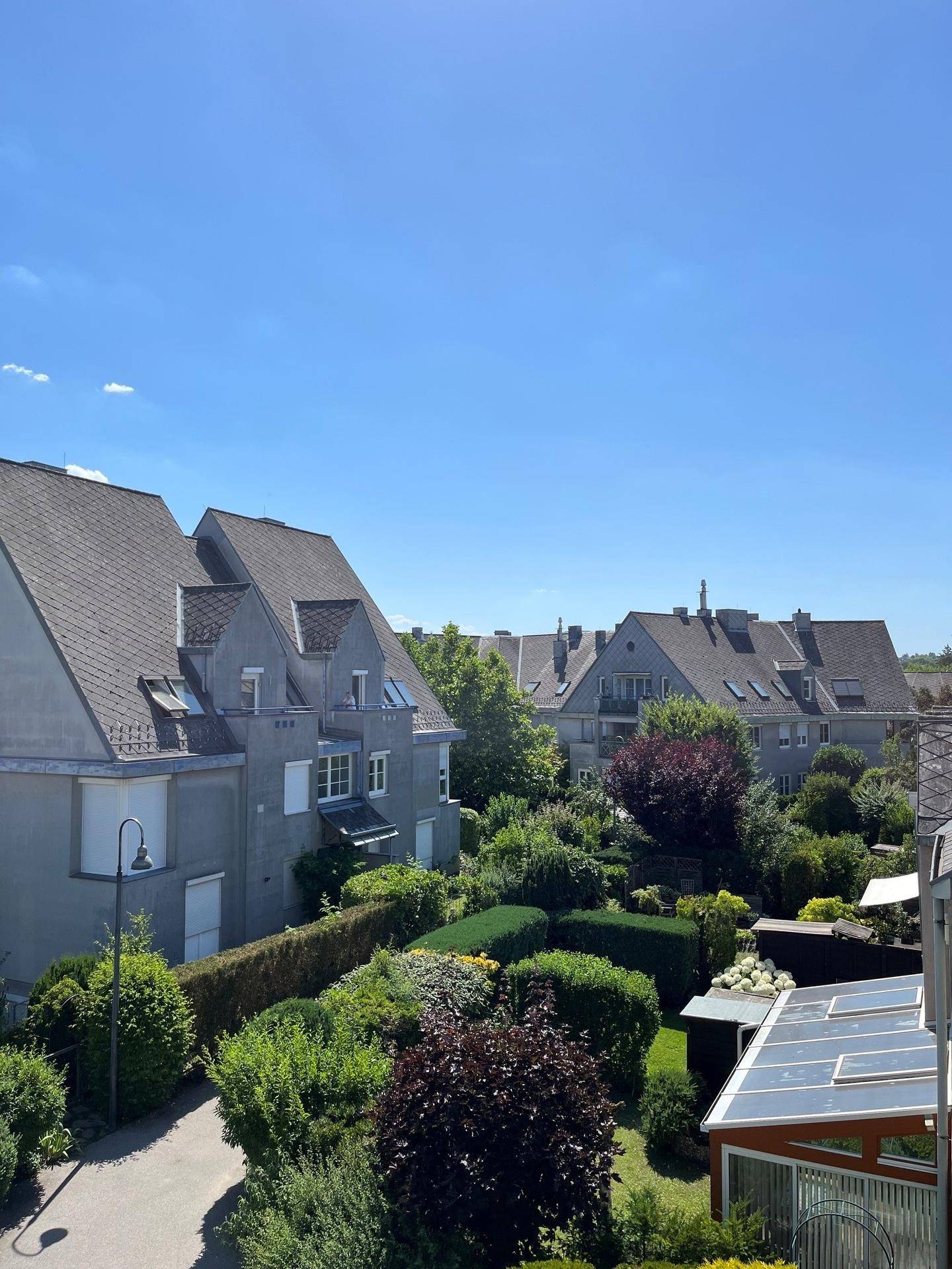 Blick auf eine Wohnsiedlung mit gepflegten Gärten und traditionellen Häusern unter blauem Himmel.