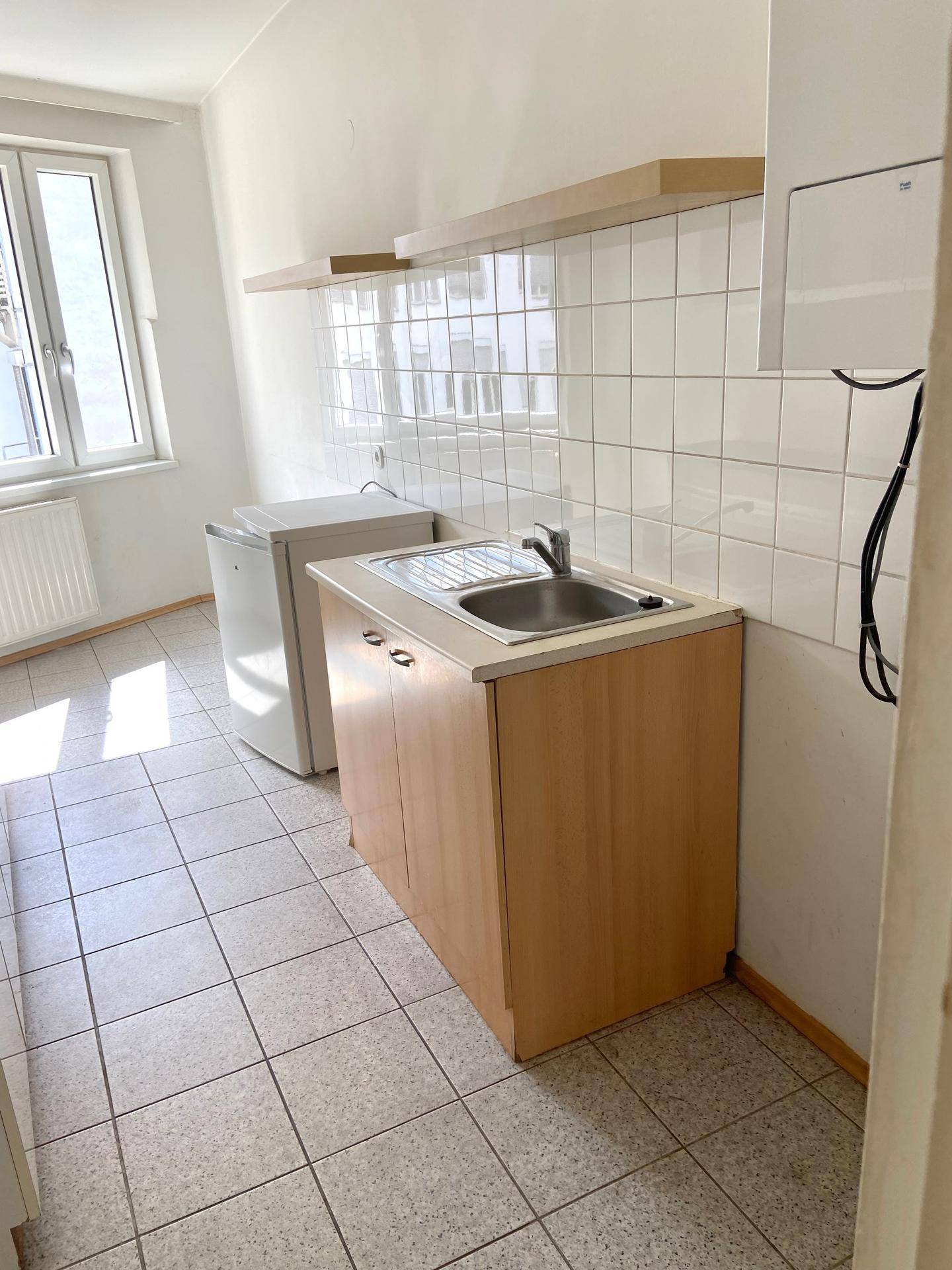 Einfache Küche mit Spülbecken, Kühlschrank und Waschmaschine, gefliestem Boden und Fenster.