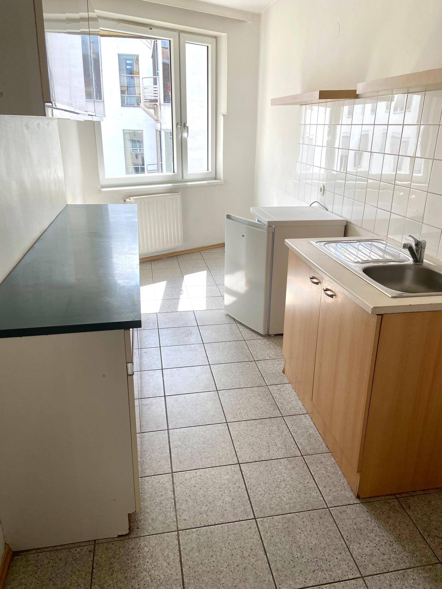 Funktionale Küche mit Spüle, Unterbauschränken, Kühlschrank und Waschmaschine, hell durch das Fenster.