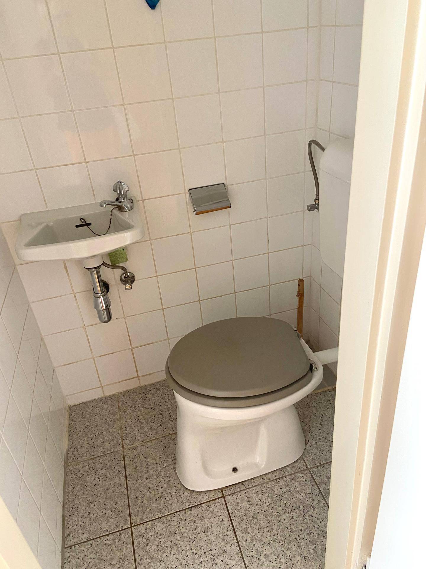 Kleines Gäste-WC mit Toilette und Handwaschbecken, komplett gefliest in Weiß und Grau.
