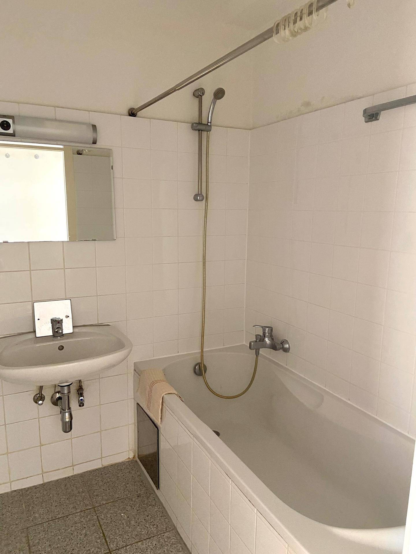 Badezimmer mit Badewanne, Duschvorrichtung und Waschbecken mit Spiegel, weiß gefliest.