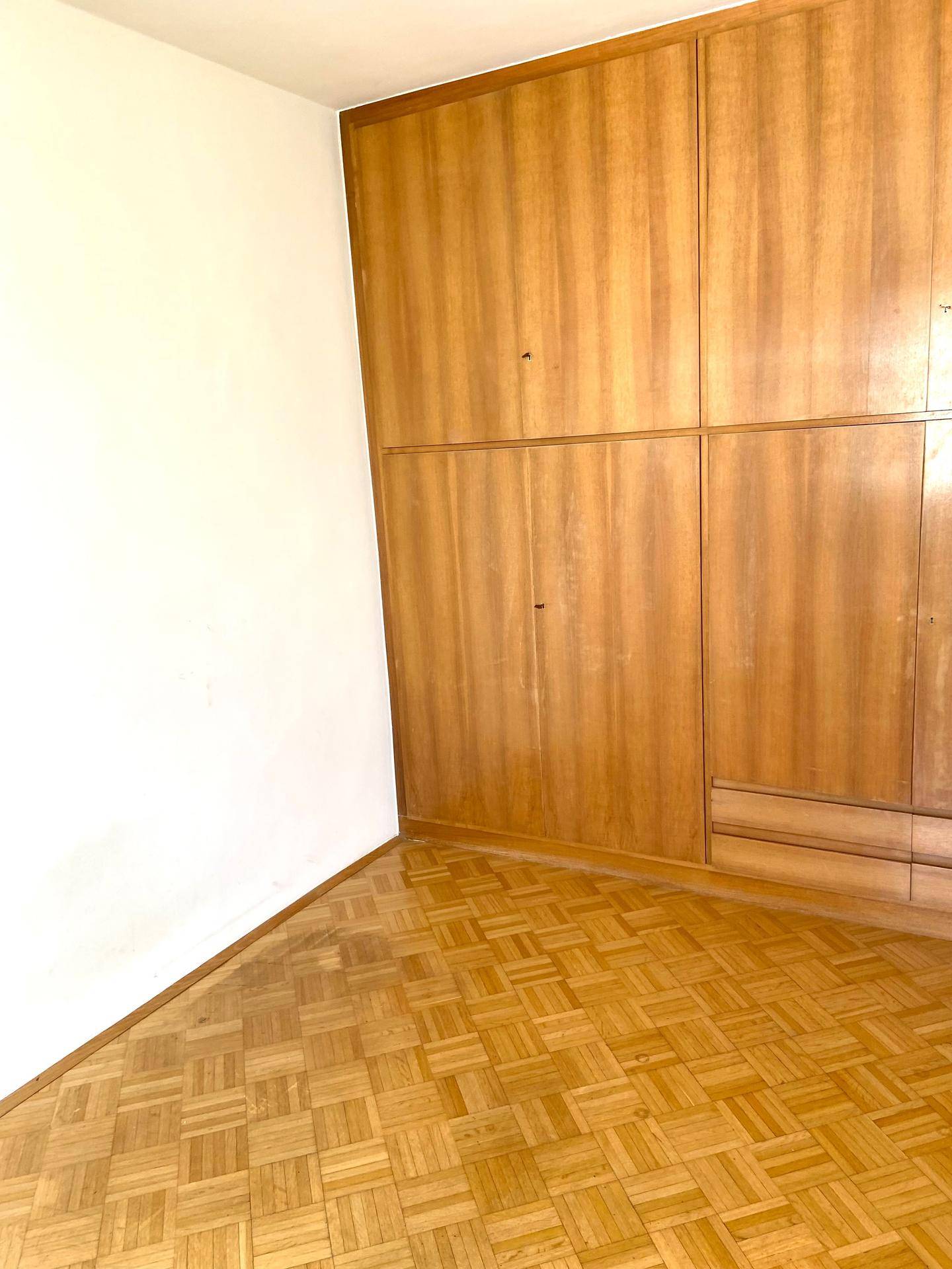 Leeres Schlafzimmer mit Fischgrätparkettboden und einem großen, eingebauten Holzschrank.
