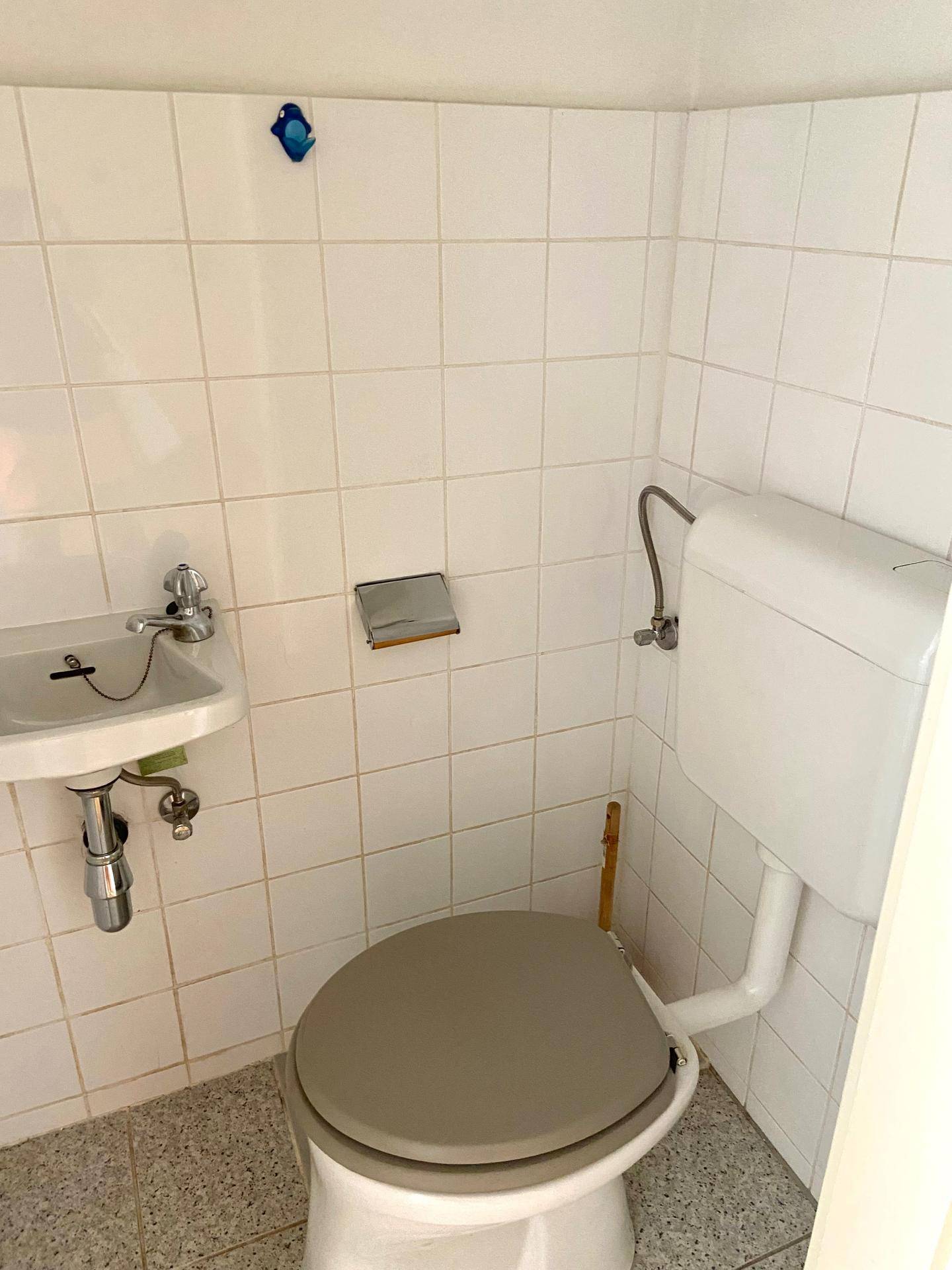 Kompaktes WC mit Toilette und kleinem Waschbecken, vollständig mit weißen Fliesen versehen.