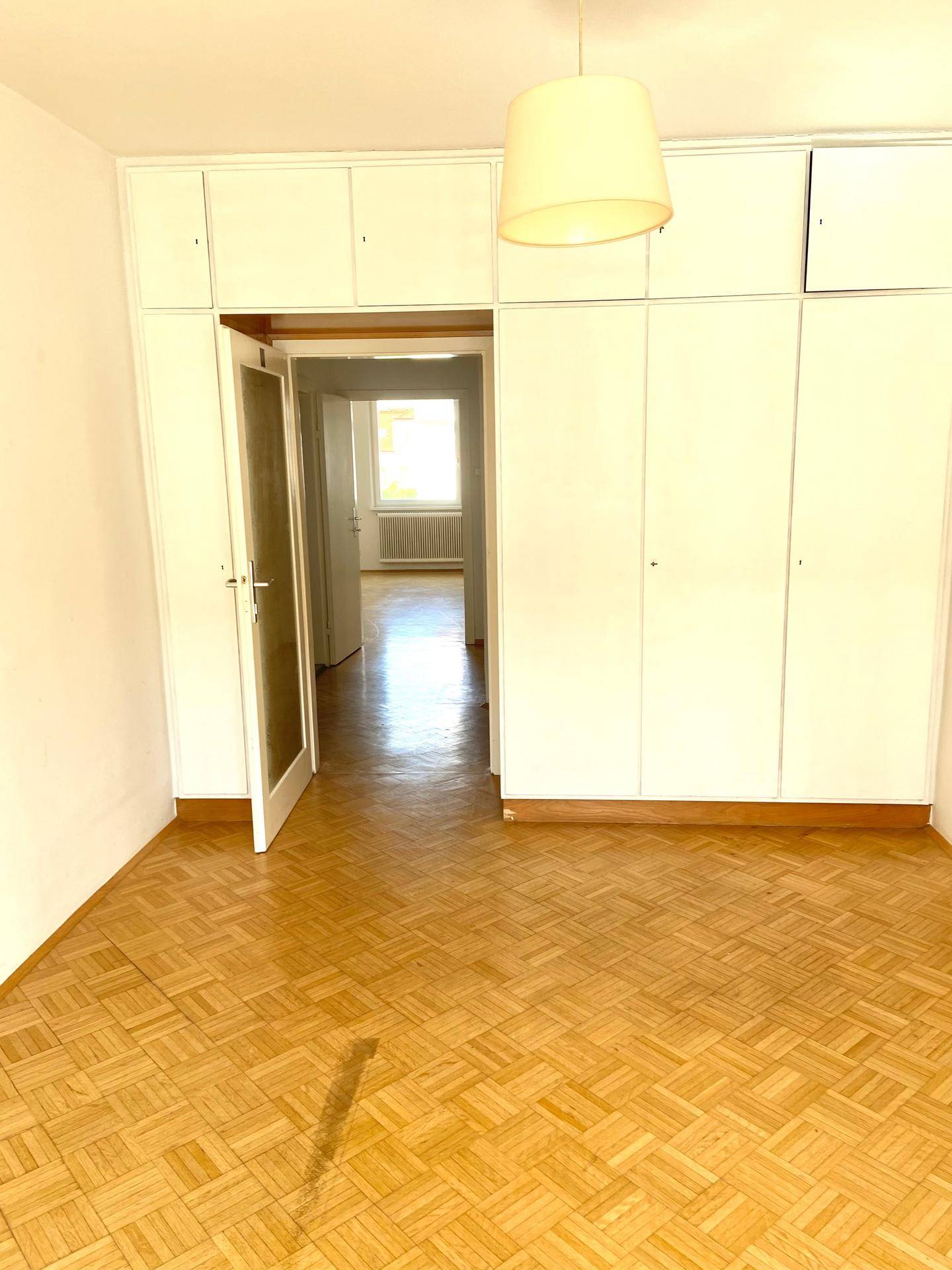 Leeres Schlafzimmer mit Fischgrätparkettboden und eingebauten weißen Kleiderschränken.