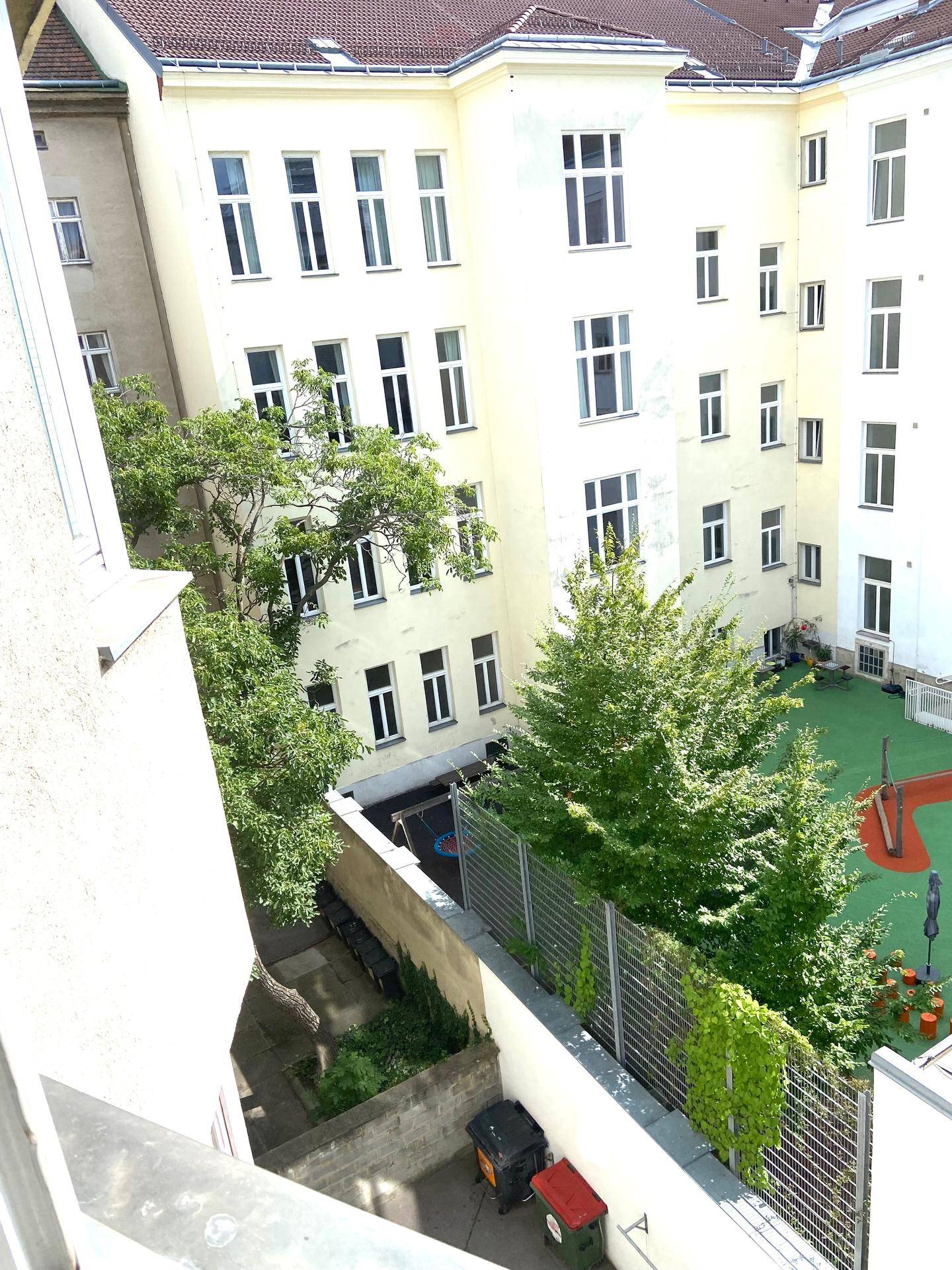 Blick von oben in einen grünen Innenhof mit Spielplatz und umliegenden Gebäudefassaden.