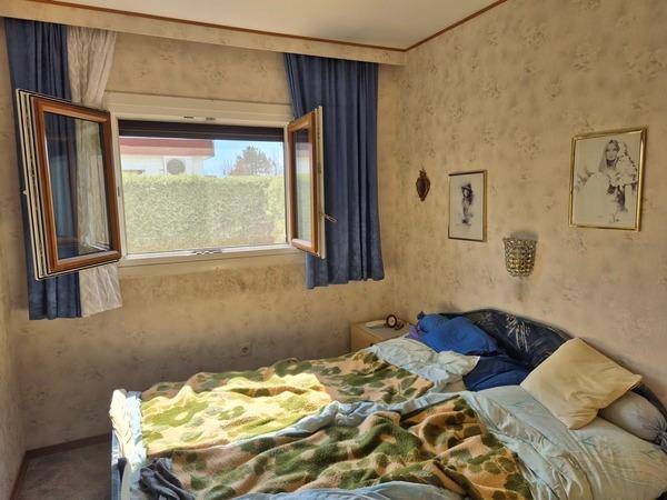 Helles Schlafzimmer mit Doppelbett, Fenster und einfacher Tapete, typisch für ein älteres Gebäude.