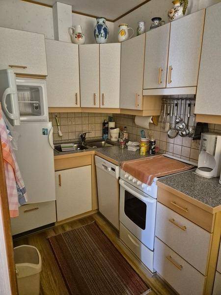 Kleine, funktionale Küche mit hellen Einbauschränken, Spüle, Herd und Kühlschrank.
