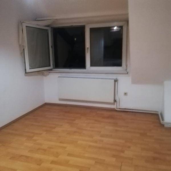 Helles Dachzimmer mit Holzboden, schrägen Wänden und einem großen Fenster für viel Licht.